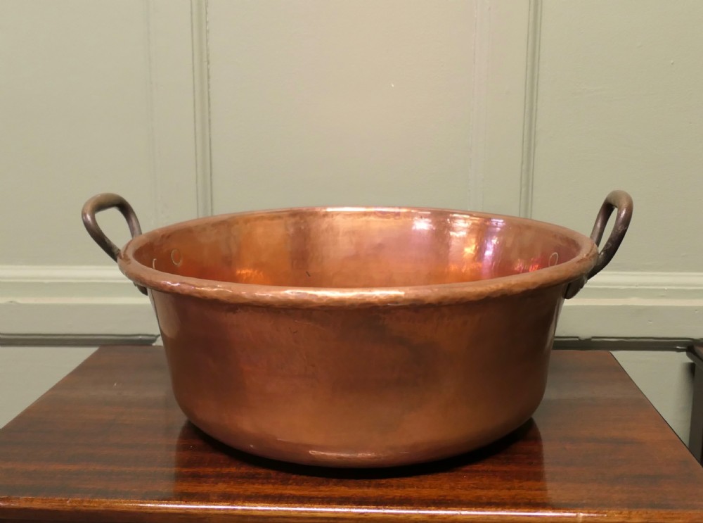 A large nineteenth-century hand-hammered copper jam pan with two cast side handles resting on a dark wood surface.