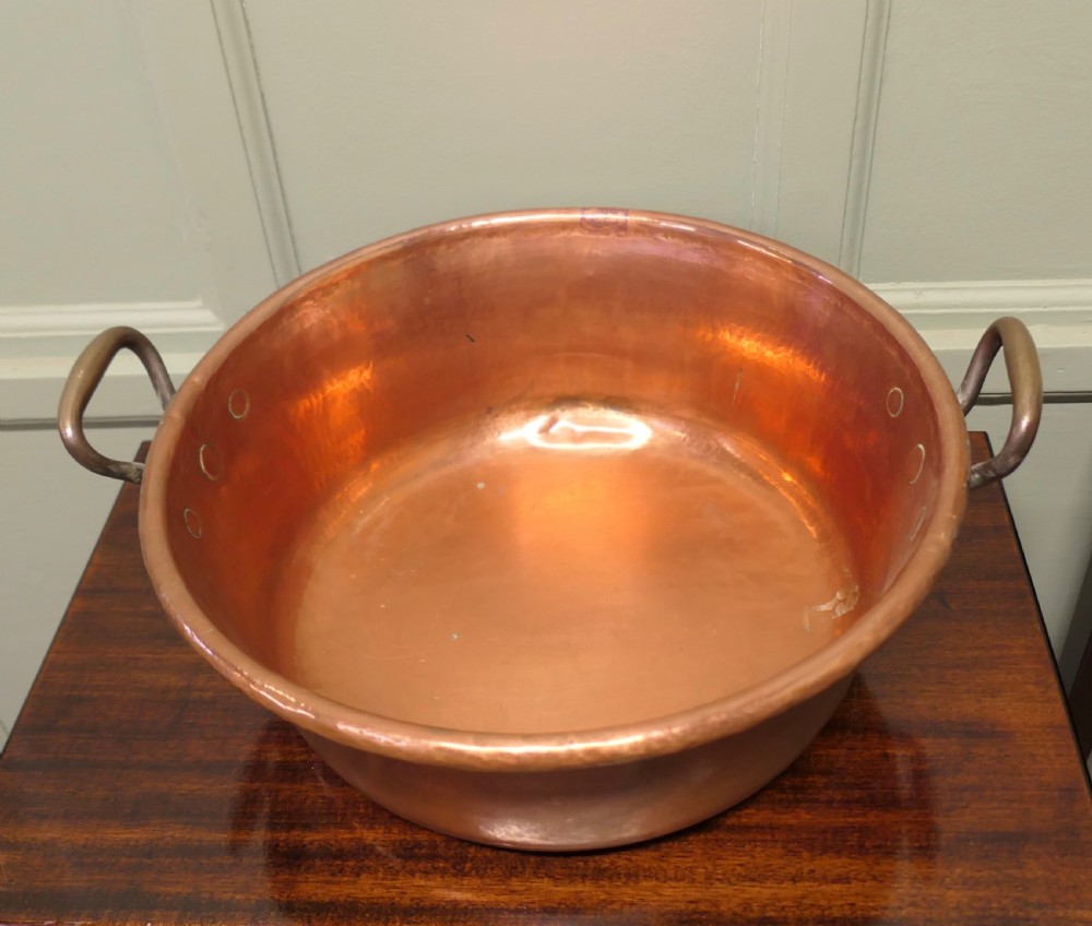 A large nineteenth-century hand-hammered copper jam pan with two cast side handles resting on a dark wood surface. View II