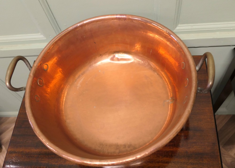 A large nineteenth-century hand-hammered copper jam pan with two cast side handles resting on a dark wood surface. View III