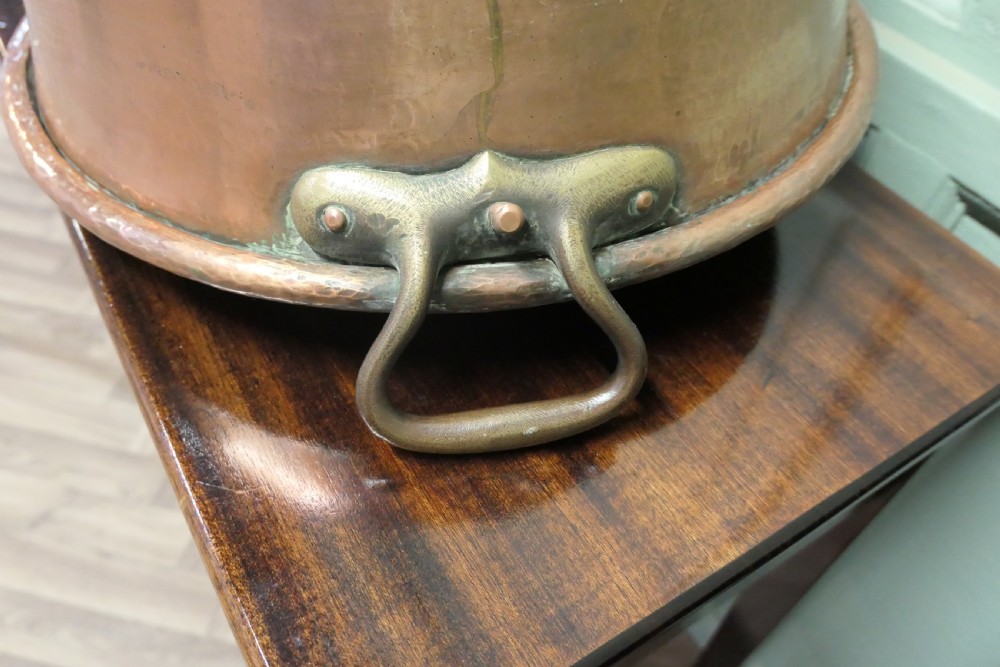 A large nineteenth-century hand-hammered copper jam pan with two cast side handles resting on a dark wood surface. View IV