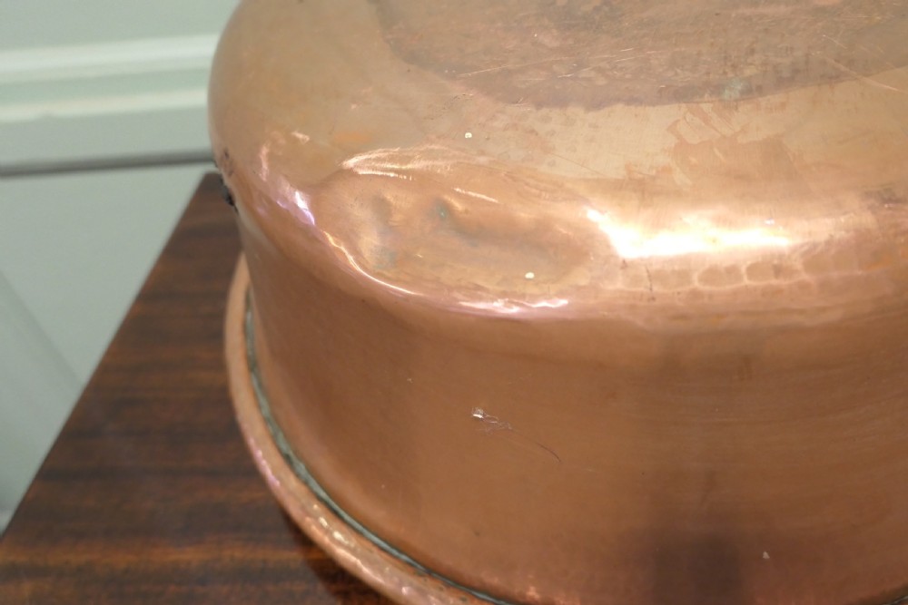 A large nineteenth-century hand-hammered copper jam pan with two cast side handles resting on a dark wood surface. View VI