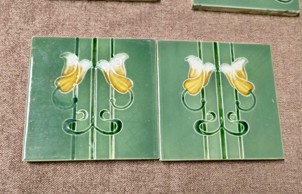 A set of eight rectangular green glazed ceramic tiles featuring embossed Art Nouveau stylised yellow and white floral motifs with curving green stems. View II