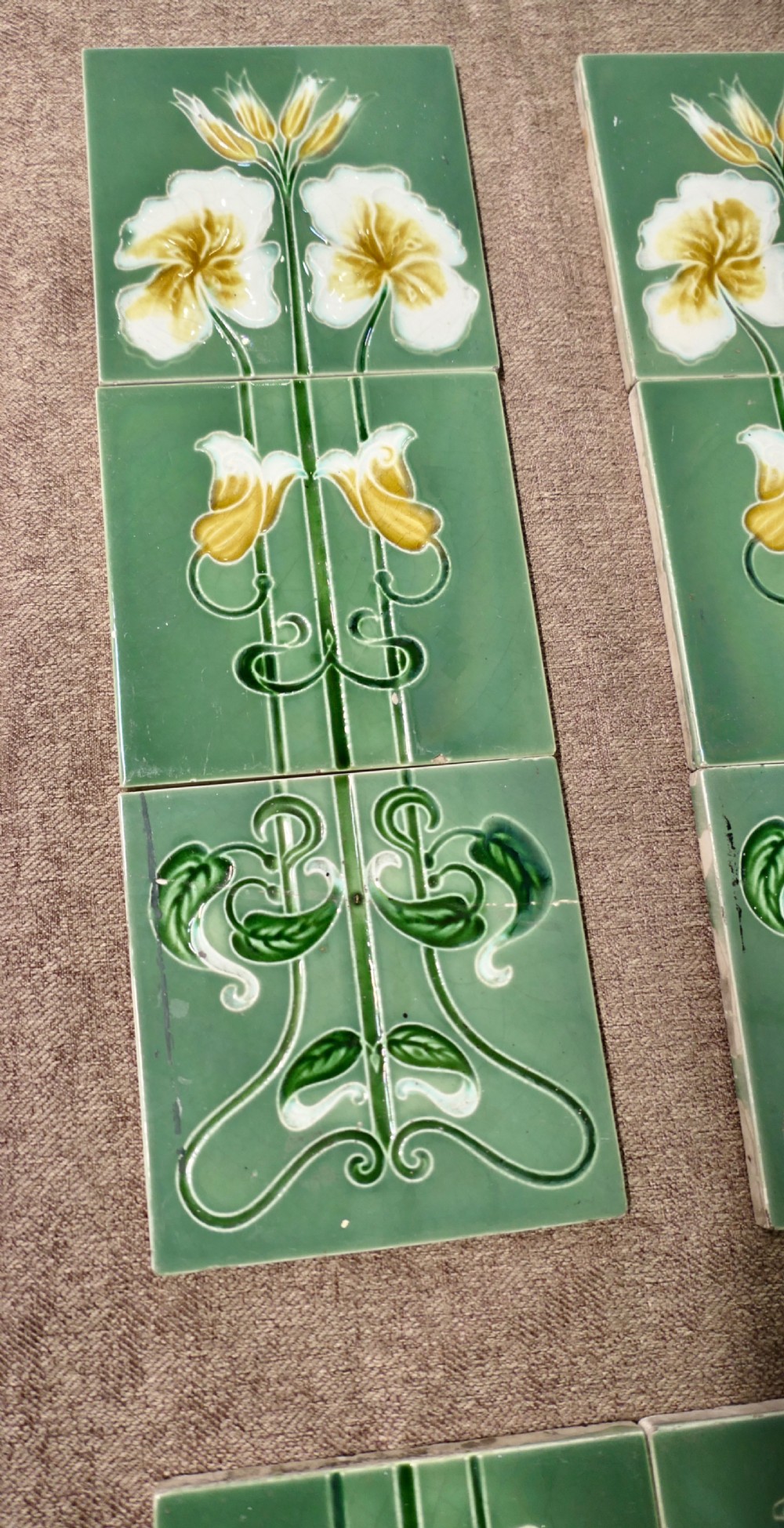 A set of eight rectangular green glazed ceramic tiles featuring embossed Art Nouveau stylised yellow and white floral motifs with curving green stems. View III