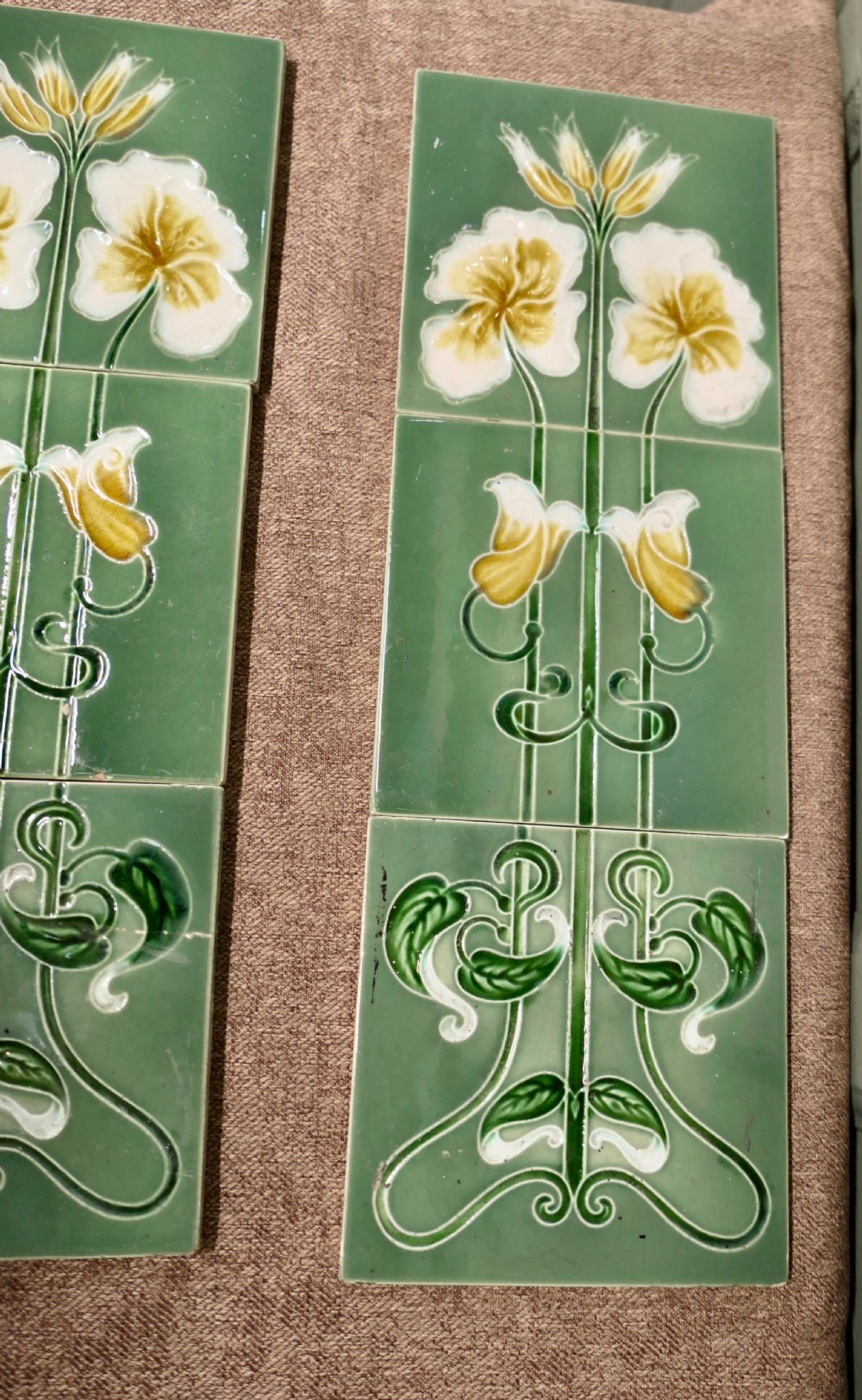 A set of eight rectangular green glazed ceramic tiles featuring embossed Art Nouveau stylised yellow and white floral motifs with curving green stems. View V