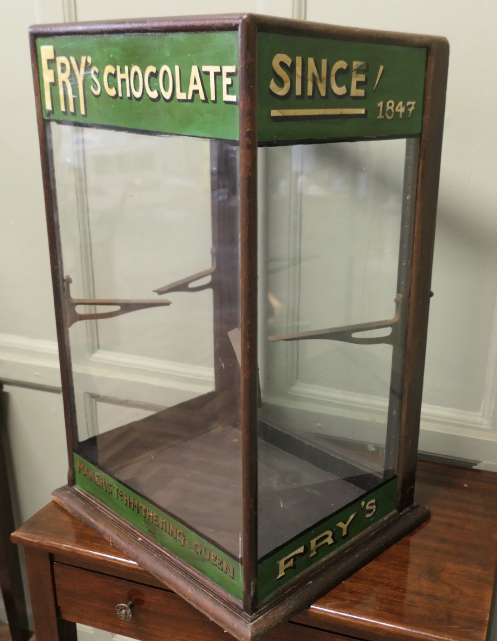An Edwardian mahogany and glass countertop display cabinet featuring green advertising panels with gold Frys Chocolate lettering. View V