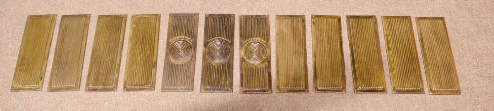 A set of twelve rectangular Art Deco brass door finger plates featuring linear reeded decoration and central concentric circle motifs.