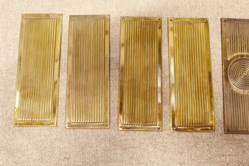 A set of twelve rectangular Art Deco brass door finger plates featuring linear reeded decoration and central concentric circle motifs. View IV