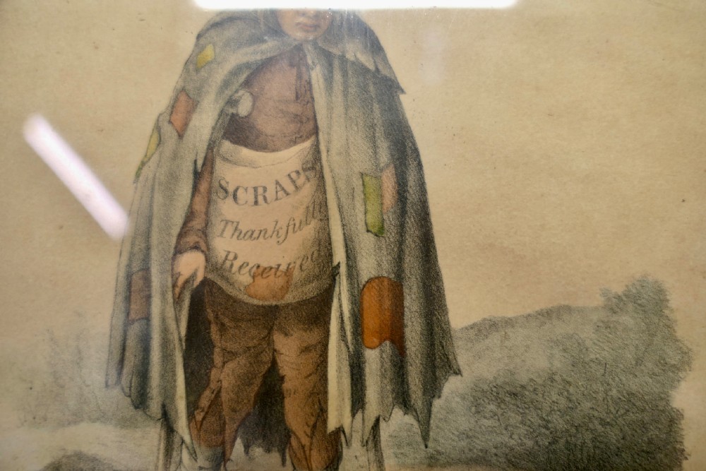 An early nineteenth-century framed hand-coloured print depicting a beggar figure with crutches and a patched cloak, titled A Thing of Shreds and Patches. View II