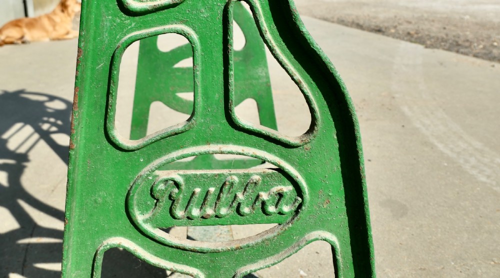 A green painted cast-iron mangle featuring an embossed Fulda logo, iron wheels, tension screws, and a hinged wooden pine top. View VII