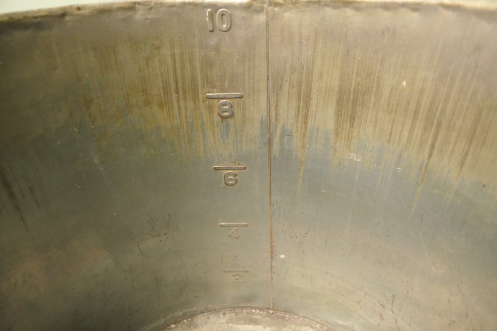 A cylindrical antique copper container featuring stamped numerical volume markings along a vertical seam. View III