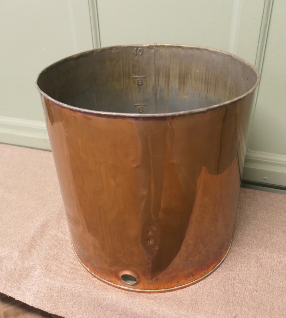 A cylindrical antique copper container featuring stamped numerical volume markings along a vertical seam. View V
