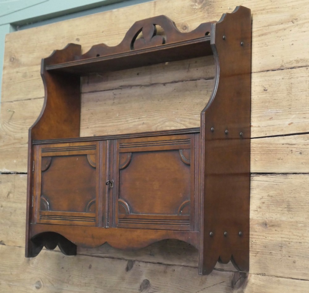 A warm brown wooden Art Deco wall cabinet featuring an upper open shelf with a pierced motif top rail above a two-door enclosed cupboard. View II