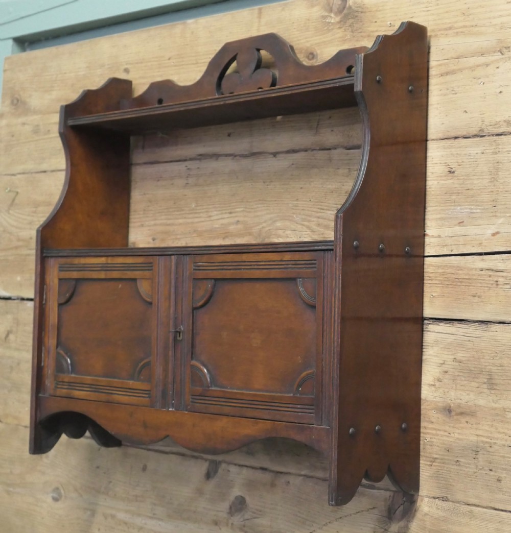 A warm brown wooden Art Deco wall cabinet featuring an upper open shelf with a pierced motif top rail above a two-door enclosed cupboard. View IV