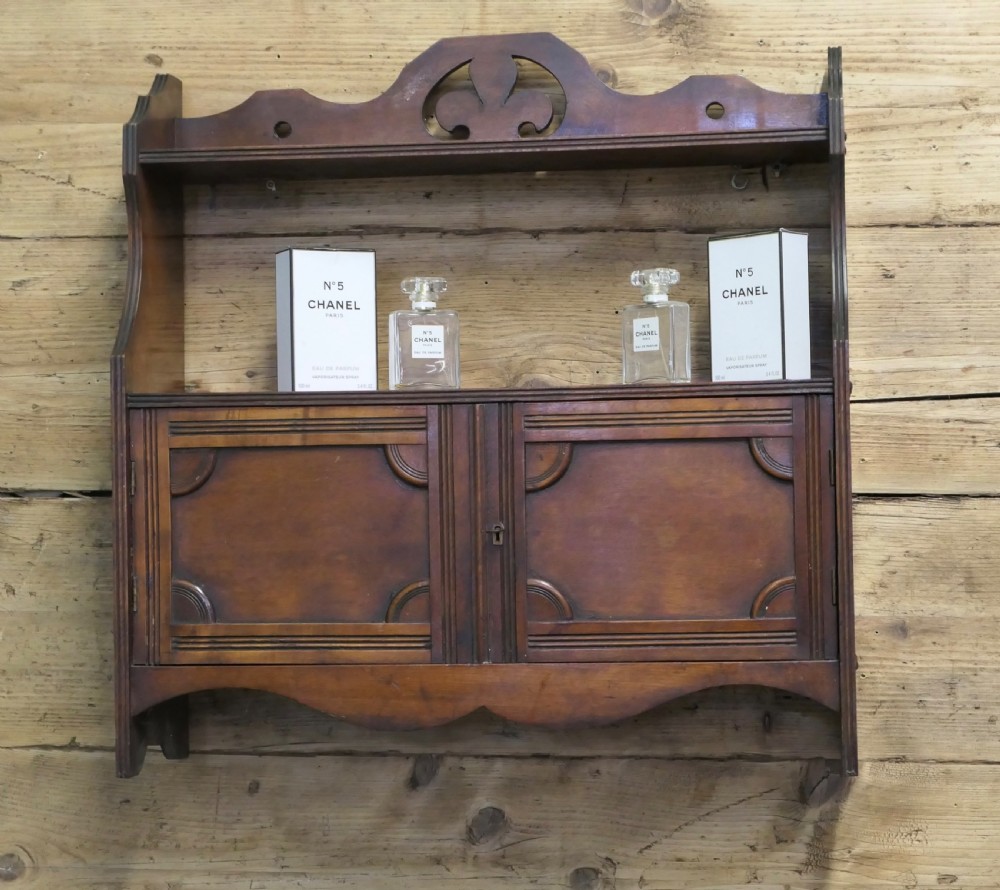 A warm brown wooden Art Deco wall cabinet featuring an upper open shelf with a pierced motif top rail above a two-door enclosed cupboard. View V