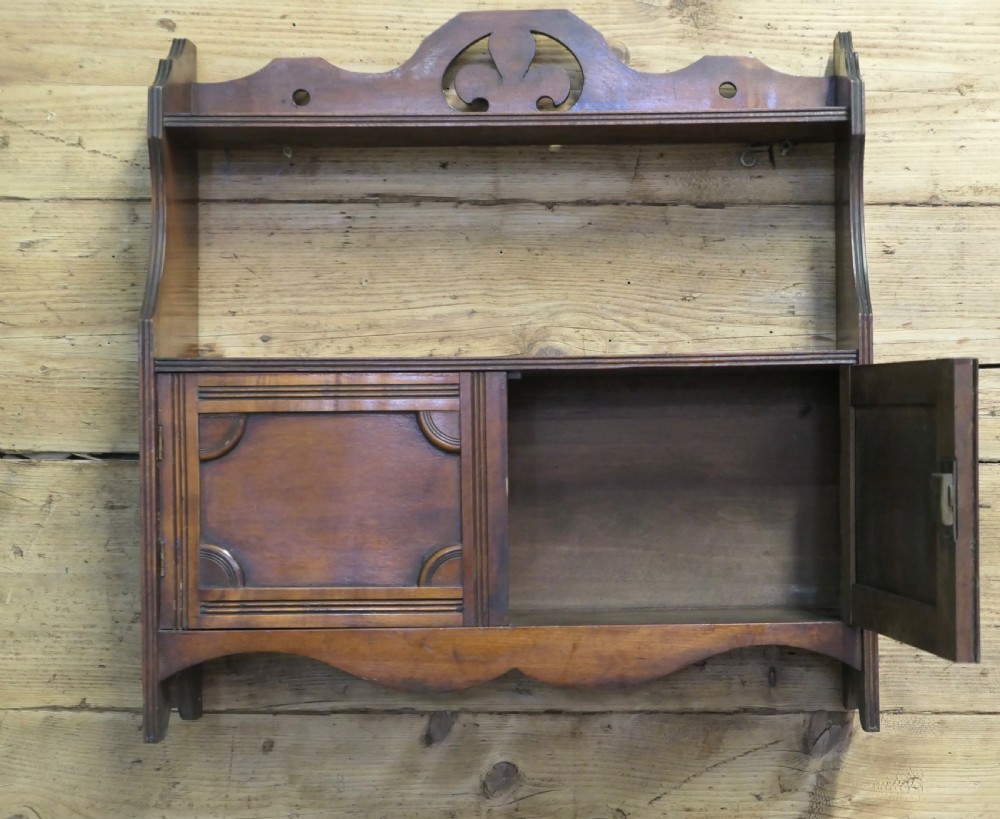 A warm brown wooden Art Deco wall cabinet featuring an upper open shelf with a pierced motif top rail above a two-door enclosed cupboard. View VI