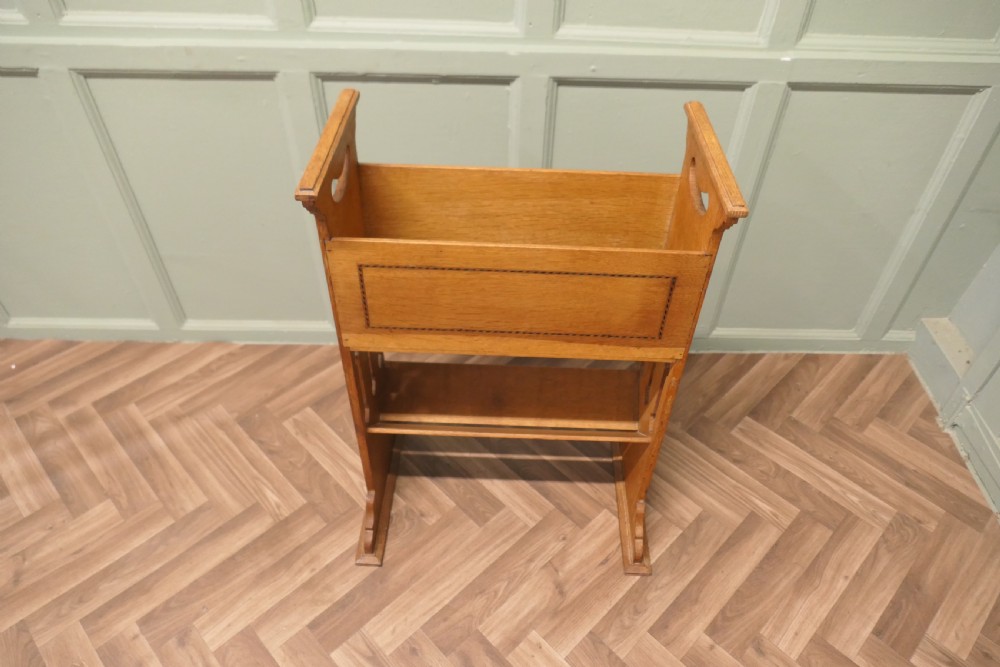 An Arts and Crafts golden oak two-tier bookcase featuring a upper trough with inlaid detail, side cut-out handles, and a lower shelf.