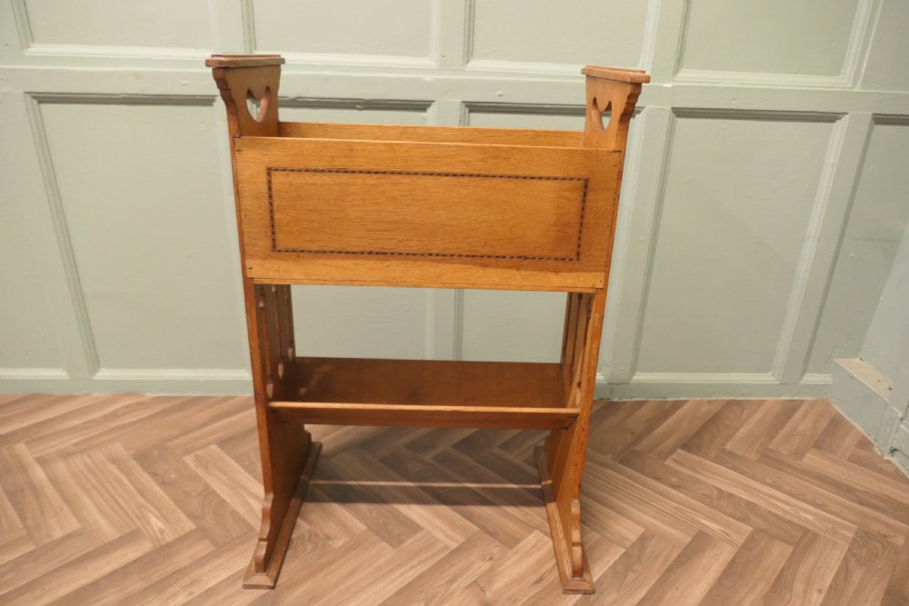 An Arts and Crafts golden oak two-tier bookcase featuring a upper trough with inlaid detail, side cut-out handles, and a lower shelf. View II