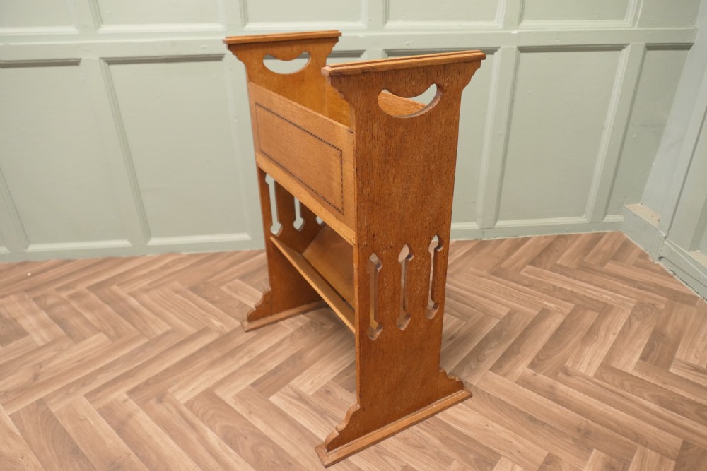 An Arts and Crafts golden oak two-tier bookcase featuring a upper trough with inlaid detail, side cut-out handles, and a lower shelf. View III