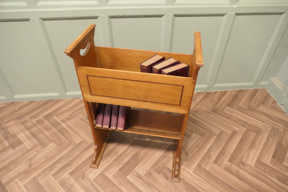 An Arts and Crafts golden oak two-tier bookcase featuring a upper trough with inlaid detail, side cut-out handles, and a lower shelf. View VII
