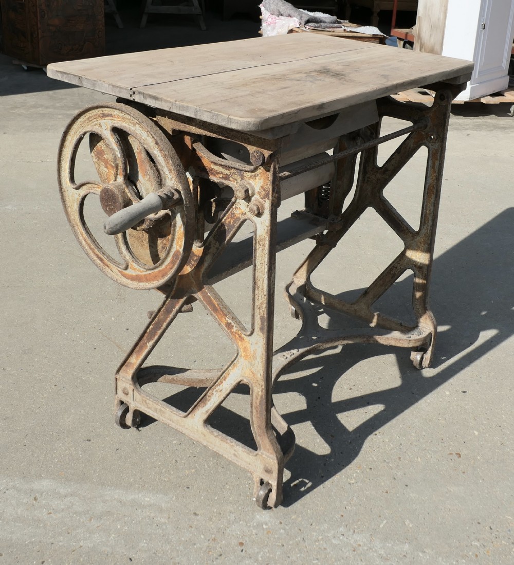 An antique cast-iron laundry mangle base with a hand-crank wheel and wooden rollers, topped with a flat pine surface.