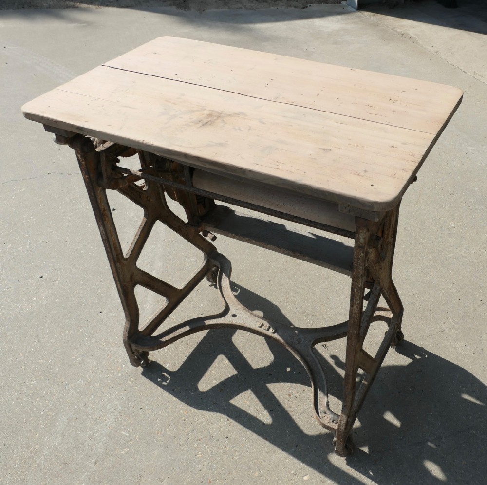 An antique cast-iron laundry mangle base with a hand-crank wheel and wooden rollers, topped with a flat pine surface. View III