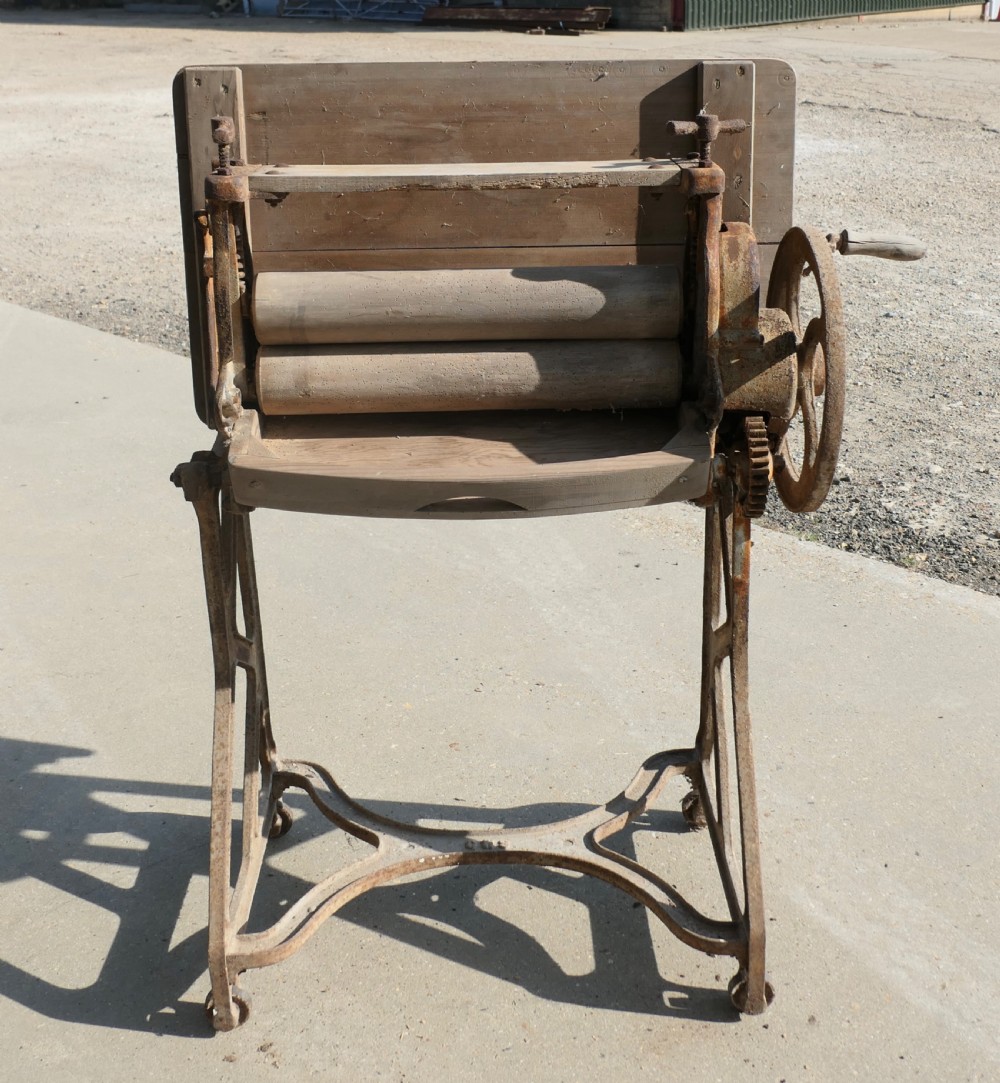 An antique cast-iron laundry mangle base with a hand-crank wheel and wooden rollers, topped with a flat pine surface. View V