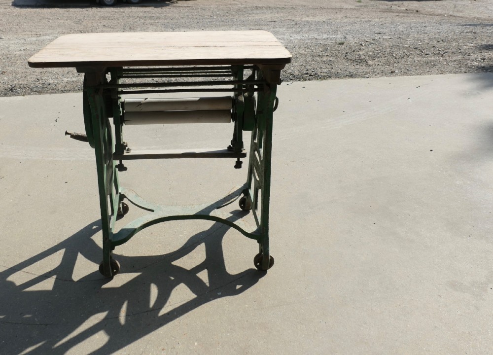 An antique cast-iron laundry mangle base with a hand-crank wheel and wooden rollers, topped with a flat pine surface. View VII