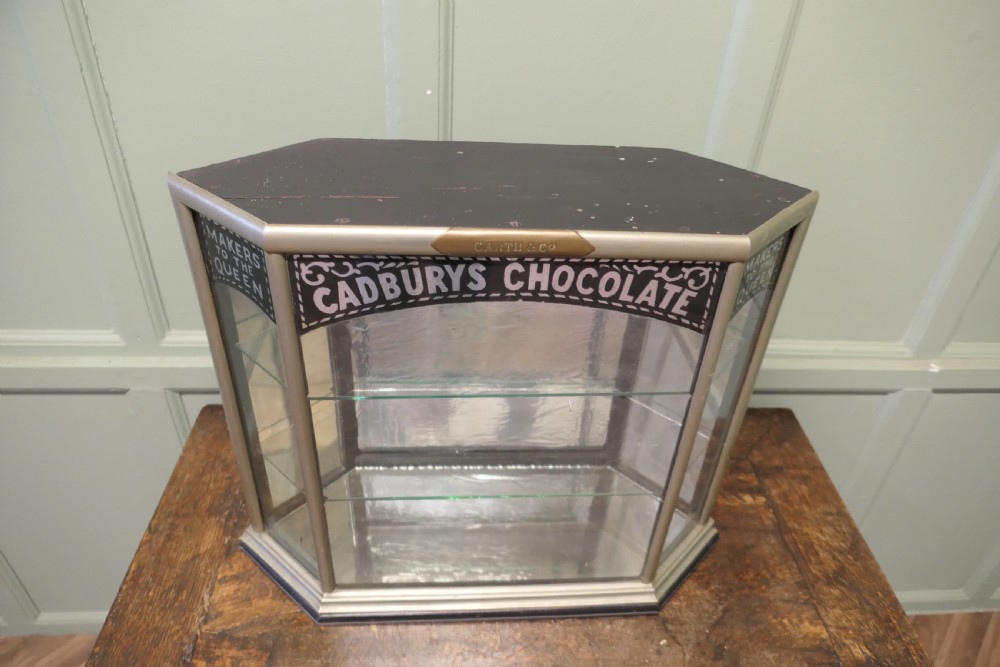 An Art Deco three-sided glass shop counter display cabinet with nickel-plated metal framing, glass shelves, mirrored back, and branded glass lettering reading Cadburys Chocolate Makers to the Queen. View III