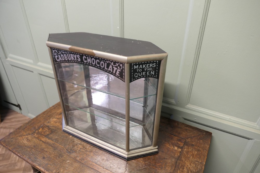 An Art Deco three-sided glass shop counter display cabinet with nickel-plated metal framing, glass shelves, mirrored back, and branded glass lettering reading Cadburys Chocolate Makers to the Queen. View V
