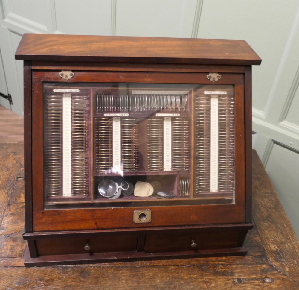 A nineteenth-century mahogany optician trial lens cabinet with a glass display door, brass fittings, and organized compartments containing optical test lenses.