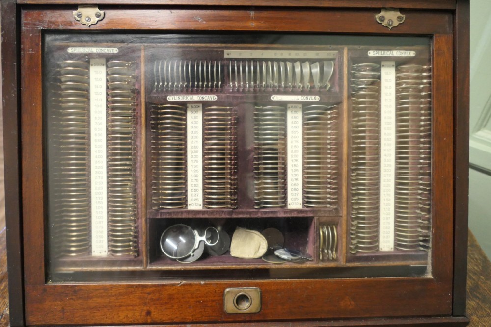 A nineteenth-century mahogany optician trial lens cabinet with a glass display door, brass fittings, and organized compartments containing optical test lenses. View III