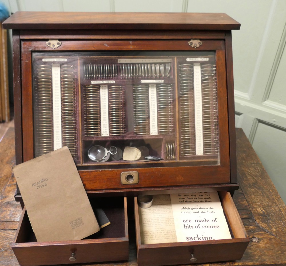 A nineteenth-century mahogany optician trial lens cabinet with a glass display door, brass fittings, and organized compartments containing optical test lenses. View VI