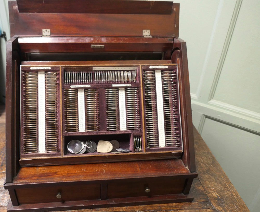 A nineteenth-century mahogany optician trial lens cabinet with a glass display door, brass fittings, and organized compartments containing optical test lenses. View VII