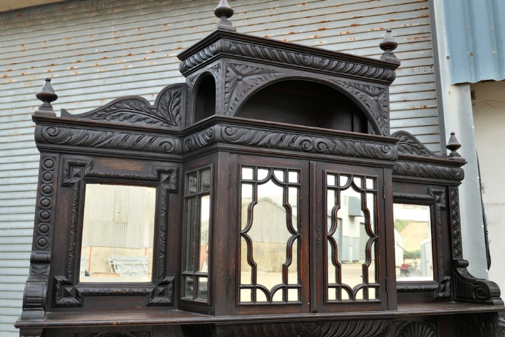 A large dark oak Victorian sideboard featuring deep Green Man carvings, a mirrored back superstructure, turned support columns, and lion head drawer handles. View III