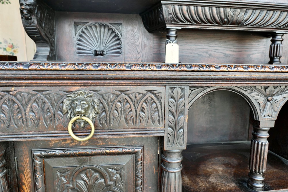 A large dark oak Victorian sideboard featuring deep Green Man carvings, a mirrored back superstructure, turned support columns, and lion head drawer handles. View IV