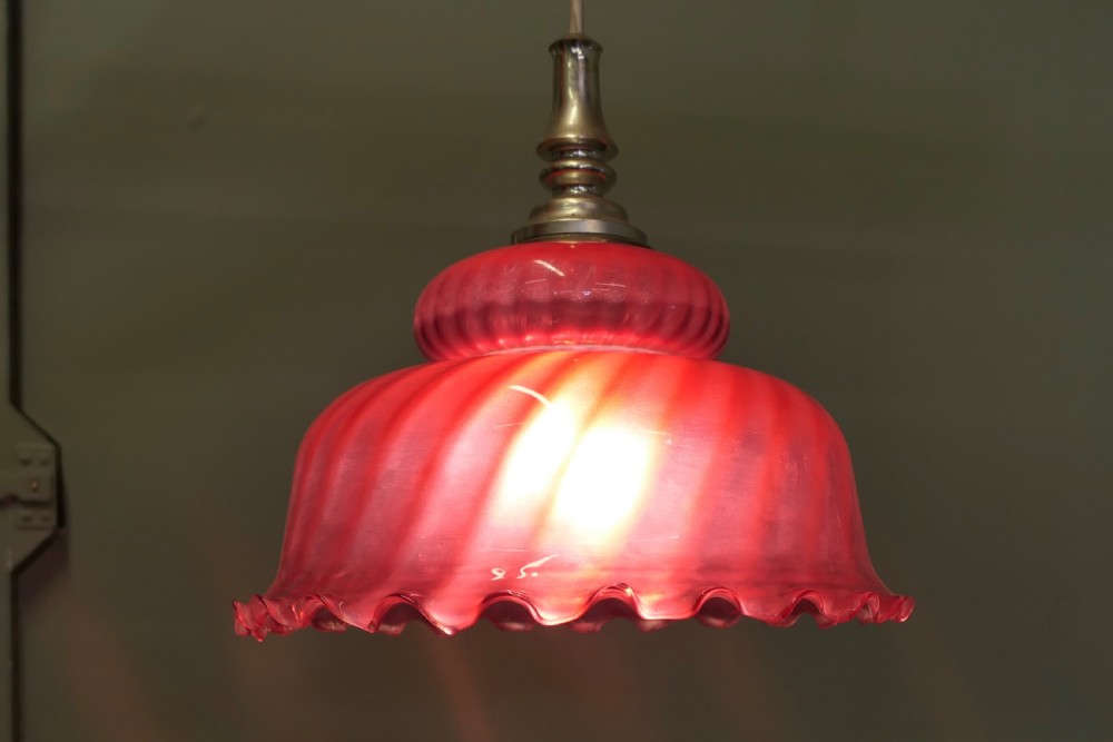 A Victorian ruby red glass pendant lampshade featuring a tiered dome shape, spiral swirled texture, ruffled lower edge, and a silver-toned metal gallery fitting. View V