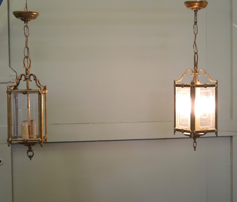 A pair of French Art Deco brass hanging lanterns featuring etched geometric glass panels and internal candle-style bulb fittings suspended from chains.