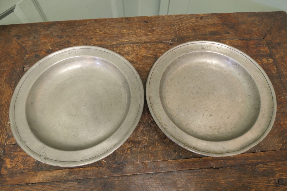 A pair of large round antique pewter charger plates with stamped initials on the rims.