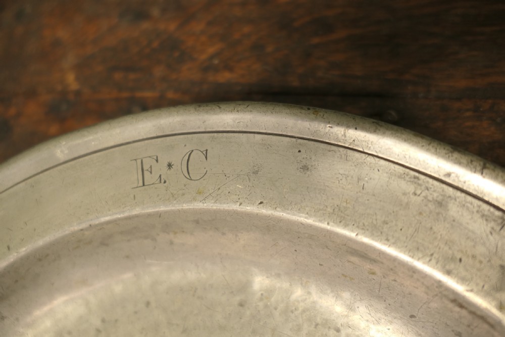A pair of large round antique pewter charger plates with stamped initials on the rims. View V