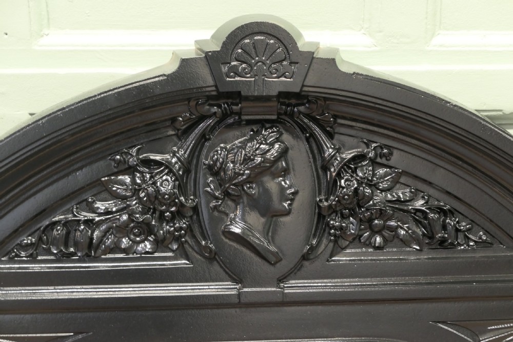 A black Victorian cast iron overmantel mirror featuring an arched pediment with a classical portrait medallion and an oval central mirror glass. View II