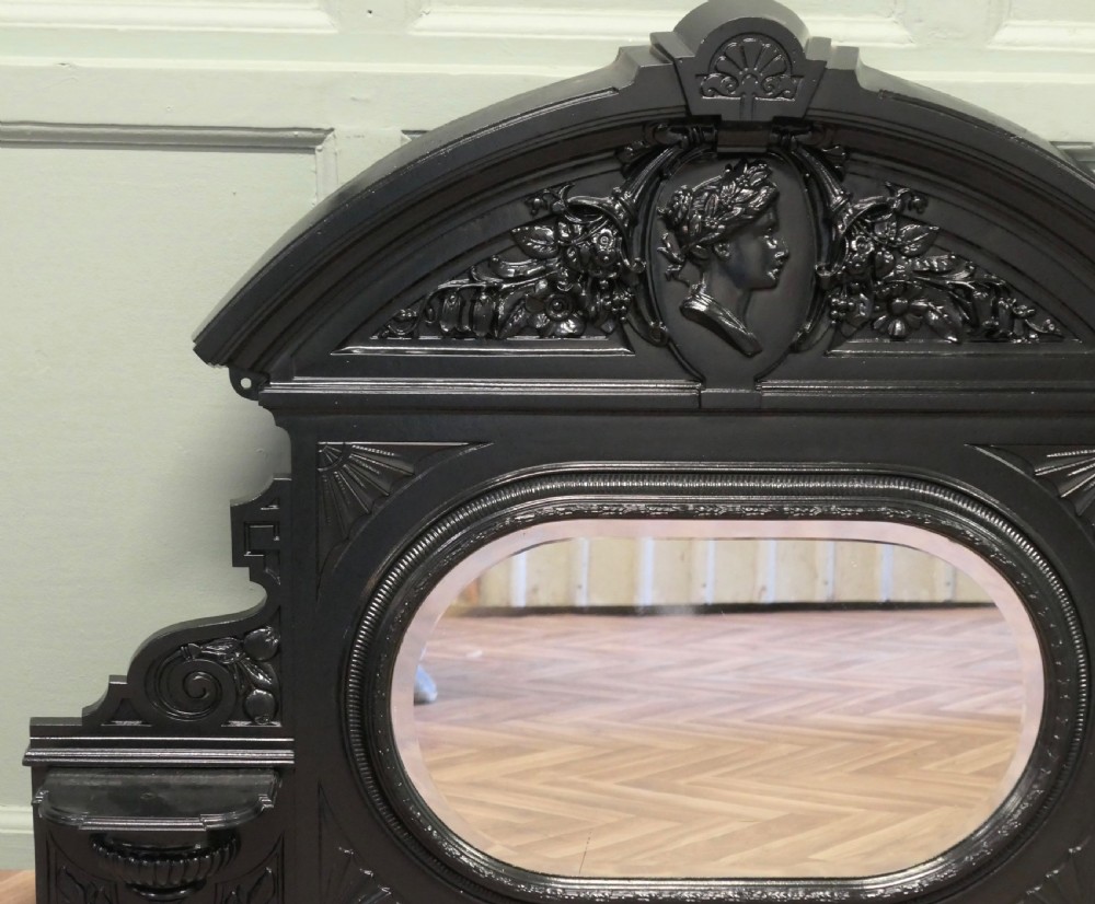 A black Victorian cast iron overmantel mirror featuring an arched pediment with a classical portrait medallion and an oval central mirror glass. View III