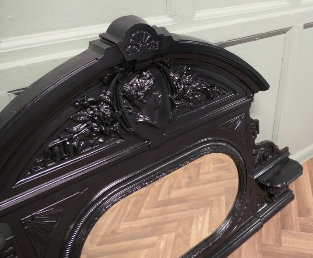A black Victorian cast iron overmantel mirror featuring an arched pediment with a classical portrait medallion and an oval central mirror glass. View IV
