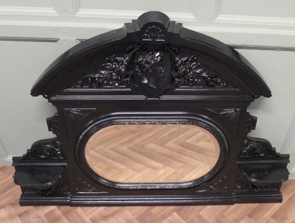 A black Victorian cast iron overmantel mirror featuring an arched pediment with a classical portrait medallion and an oval central mirror glass. View V