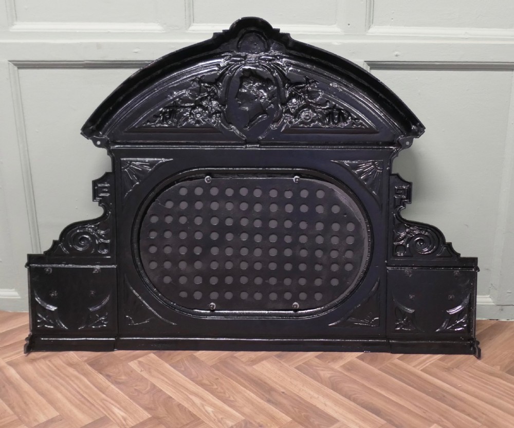A black Victorian cast iron overmantel mirror featuring an arched pediment with a classical portrait medallion and an oval central mirror glass. View VI