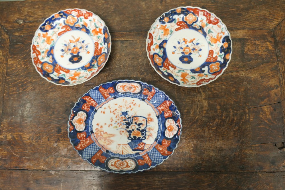 A set of three 19th-century Imari ironstone ceramic plates featuring scalloped edges and hand-painted blue, terracotta, and white floral motifs.