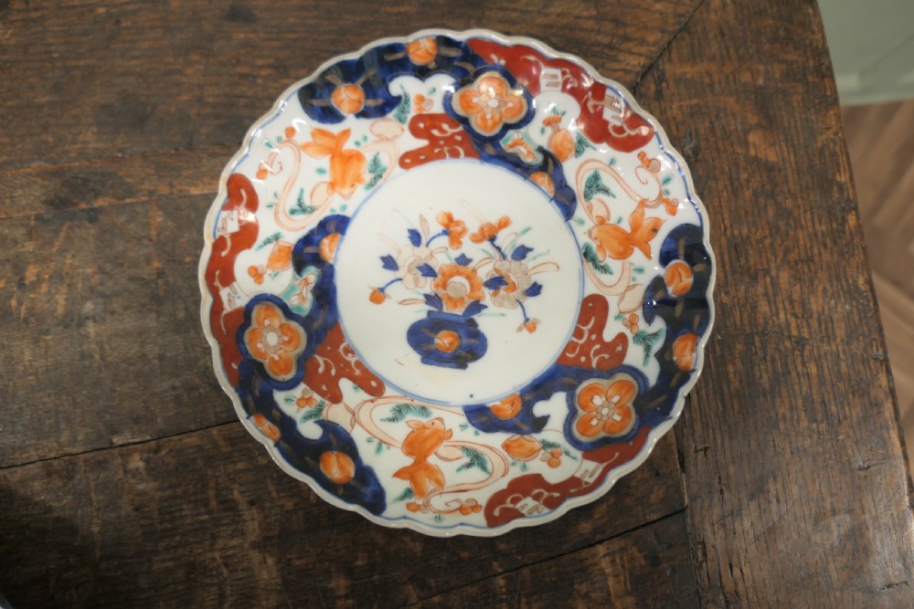 A set of three 19th-century Imari ironstone ceramic plates featuring scalloped edges and hand-painted blue, terracotta, and white floral motifs. View III