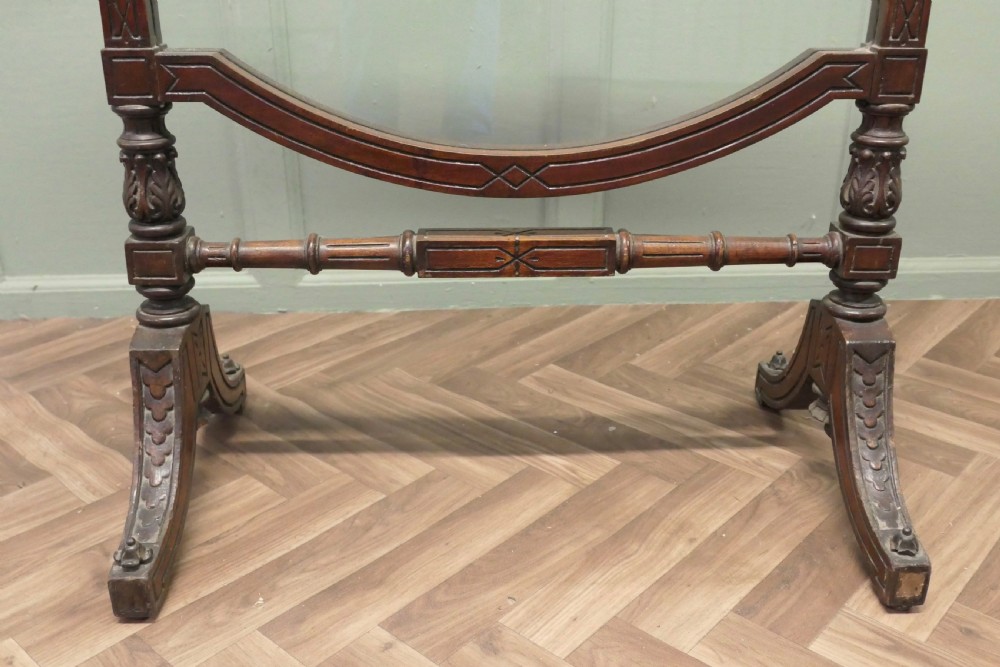 A freestanding Victorian dark mahogany fire screen featuring a clear glass panel, carved finials, turned side columns, and splayed trestle feet. View VII