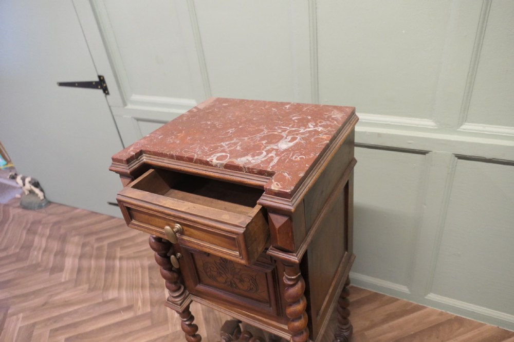 An antique French walnut night table featuring a marble top, a carved drawer, a lower cupboard door with foliate carvings, and barley twist legs. View VI