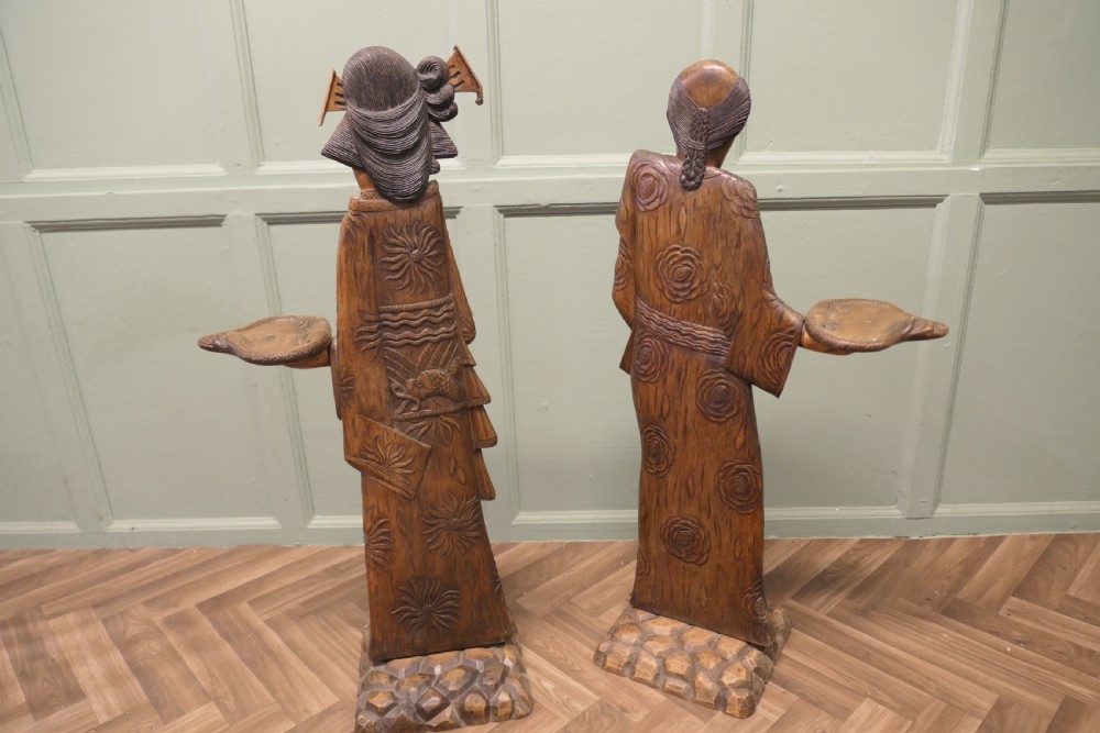 A pair of tall carved wood Japanese figures standing on stone-textured bases, each wearing detailed patterned kimonos and holding a raised tray. View II