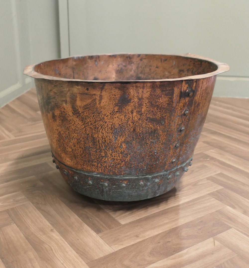 A 19th-century deep copper vessel featuring hand-riveted vertical and base seams with a wide flared rim and natural surface patina.